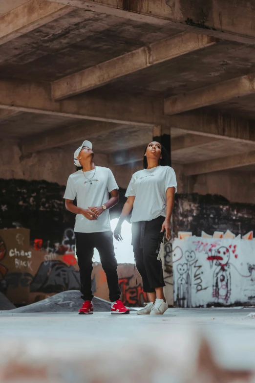 two skateboarders talking with each other under an overpass