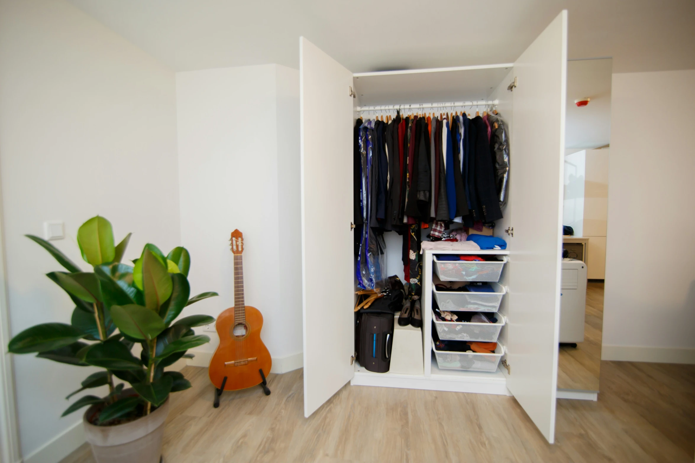 an open closet with clothes and a guitar