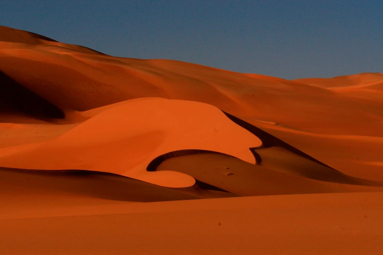 a desert with sand dunes and hills under a blue sky