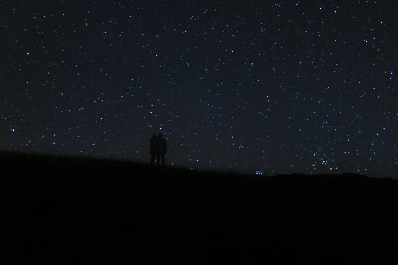 the night sky has many stars over a man standing on top of a hill