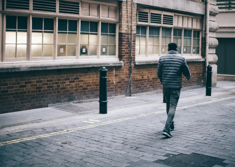 a man is walking down the sidewalk in front of an old brick building