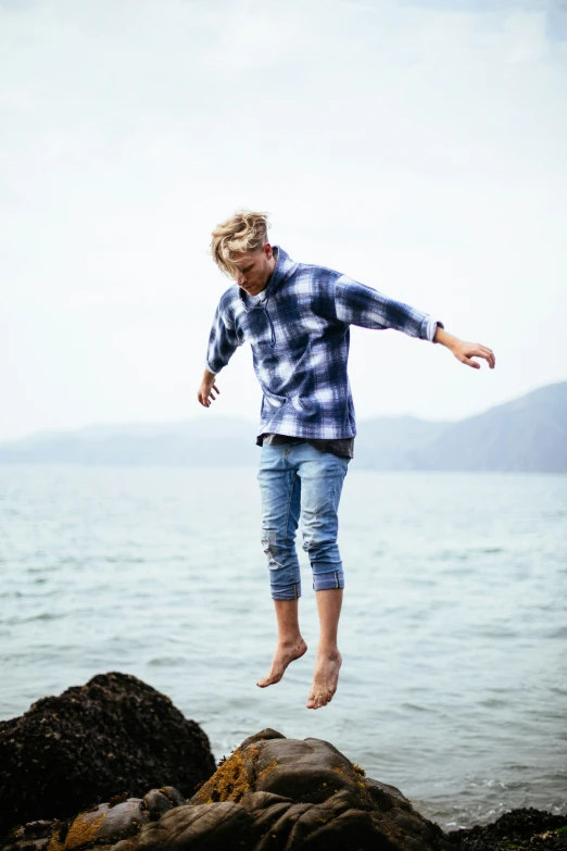 a man on the rocks jumping off of a rock into the ocean