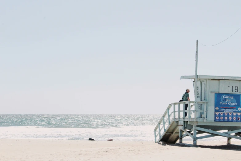 a man standing on top of a lifeguard tower next to the ocean