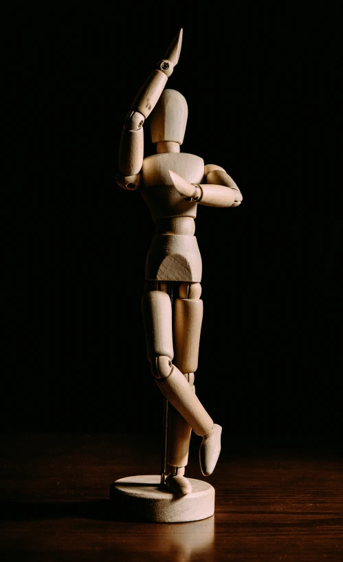 a wooden mannequin posed and gesturing in a darkened room