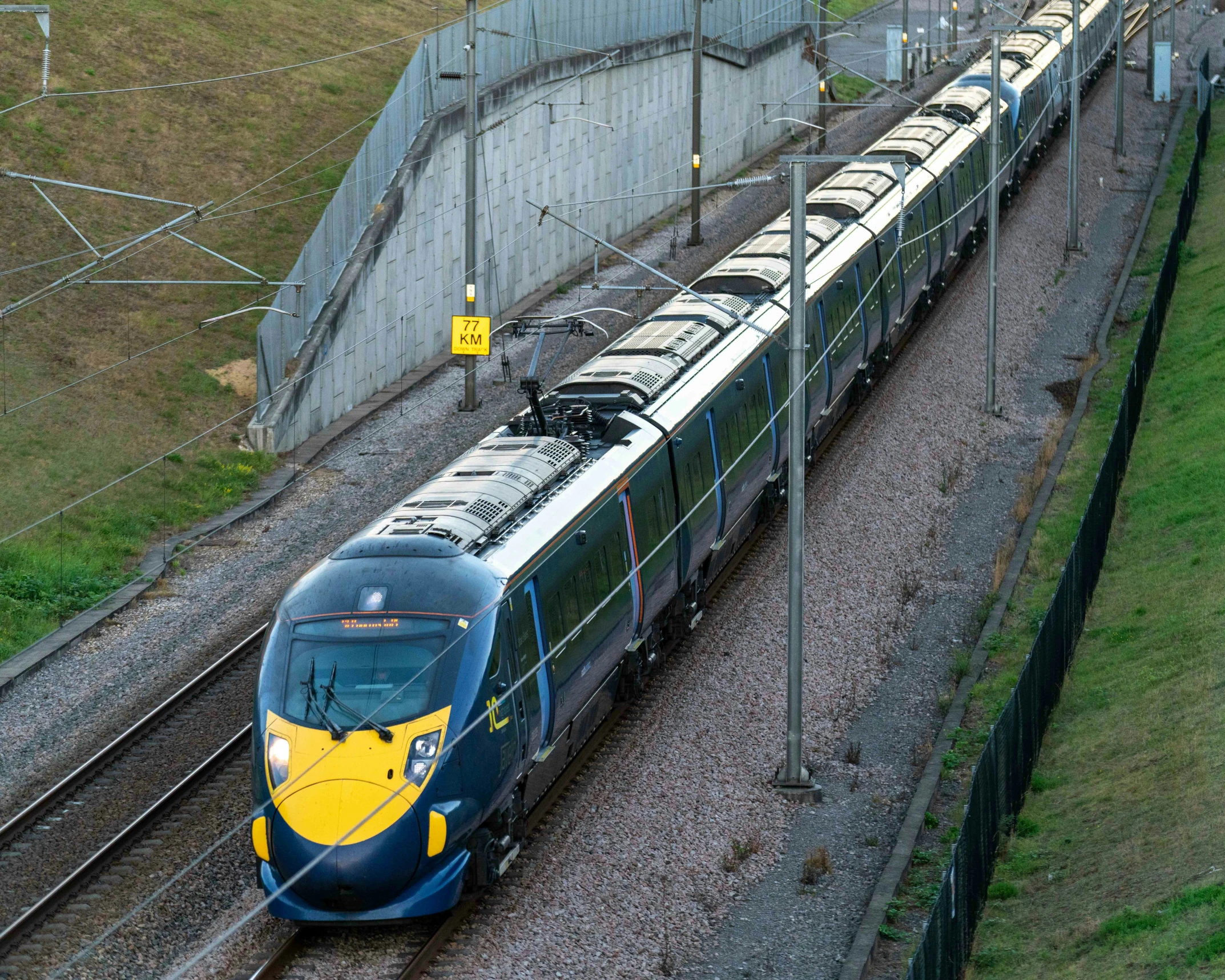 a passenger train traveling down tracks next to a tall wall