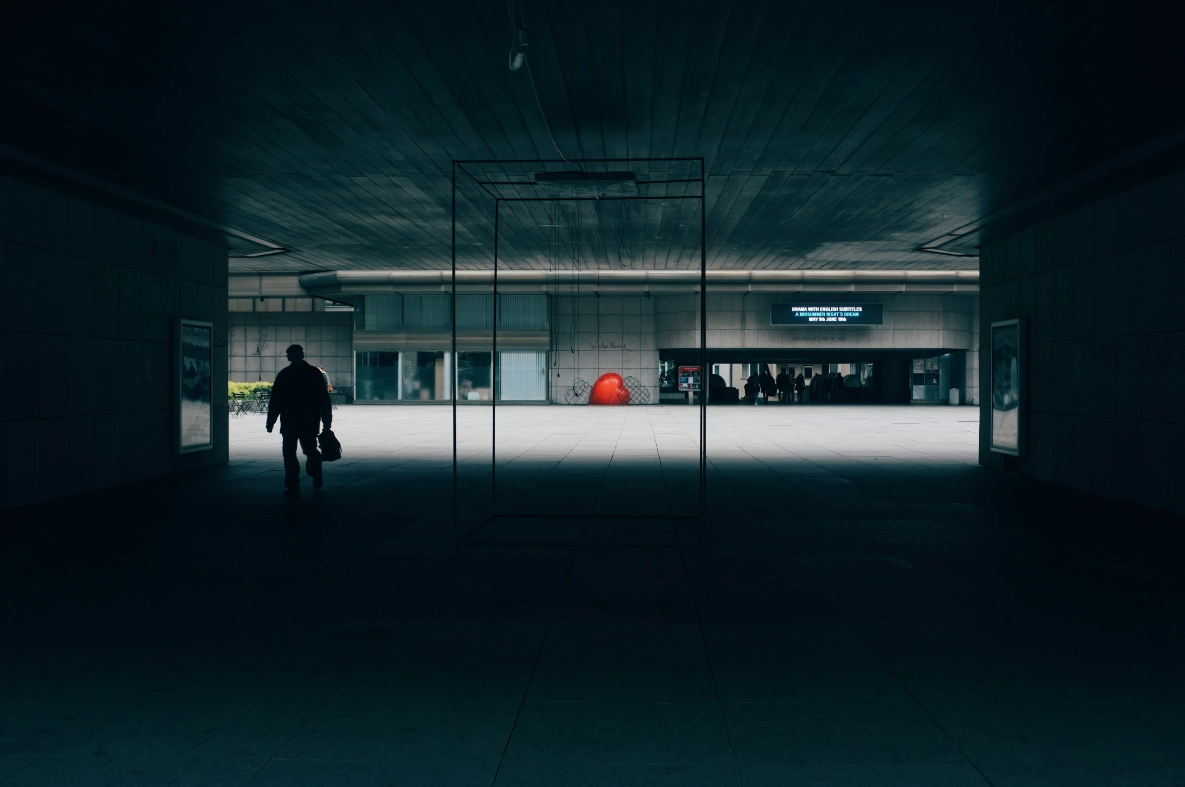 a dark room with some windows to see people walking around