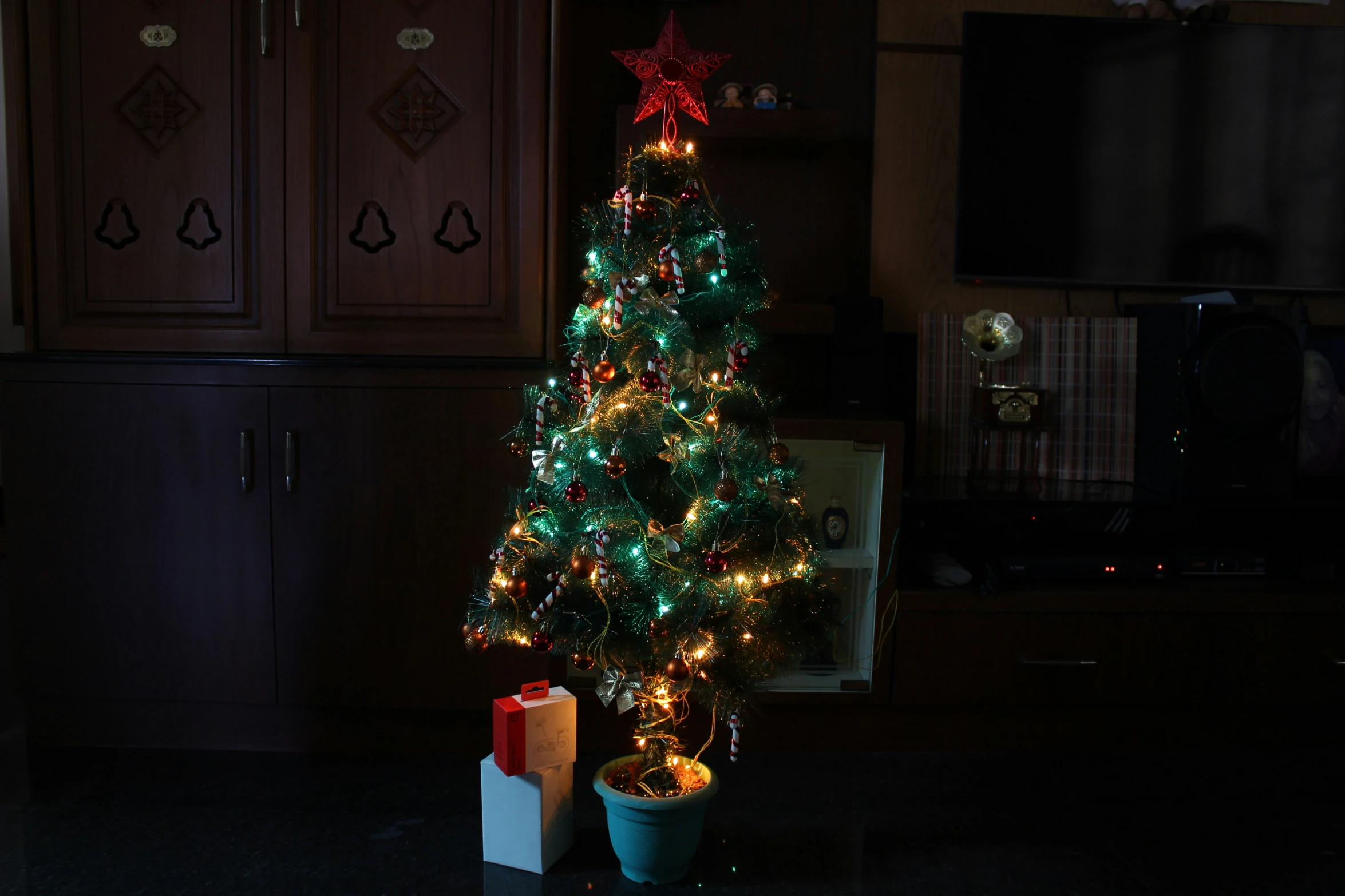 a lit christmas tree next to a christmas present on a black counter