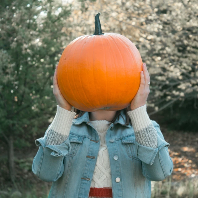 a woman holding a pumpkin with her head