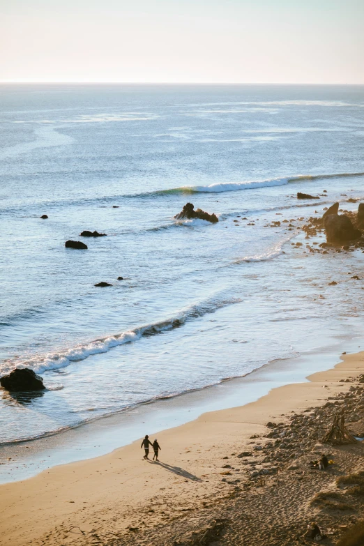 two people walking on the beach with waves coming in