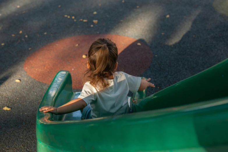 a little girl riding on the bottom of a green slide