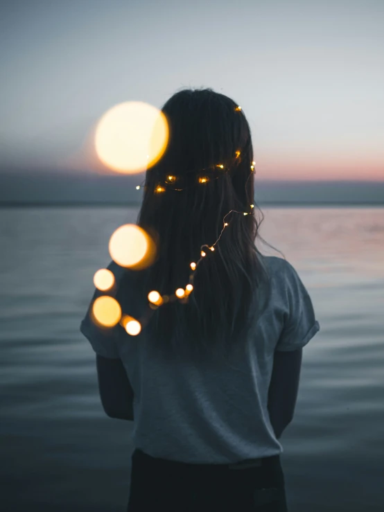 a person with many lights strung on their head in front of the ocean