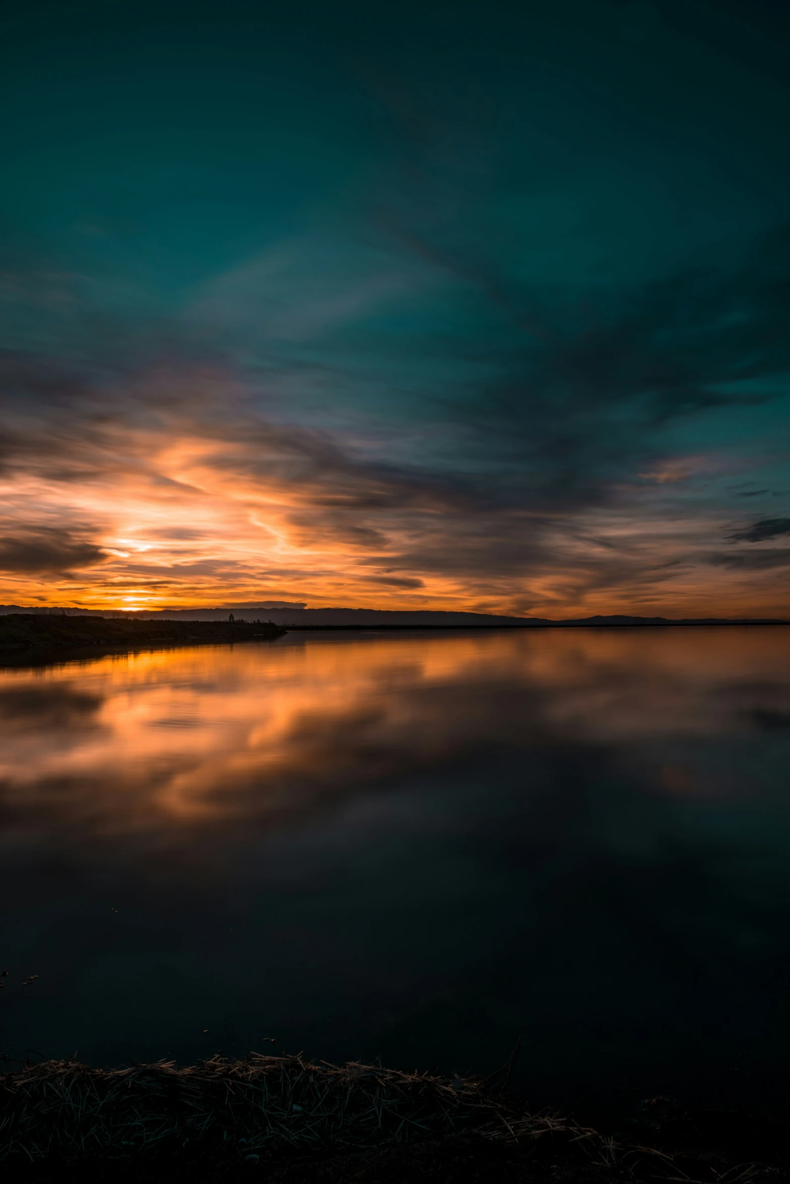 a body of water sitting under a sunset filled sky