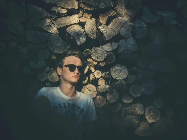 a young man in white shirt next to large logs