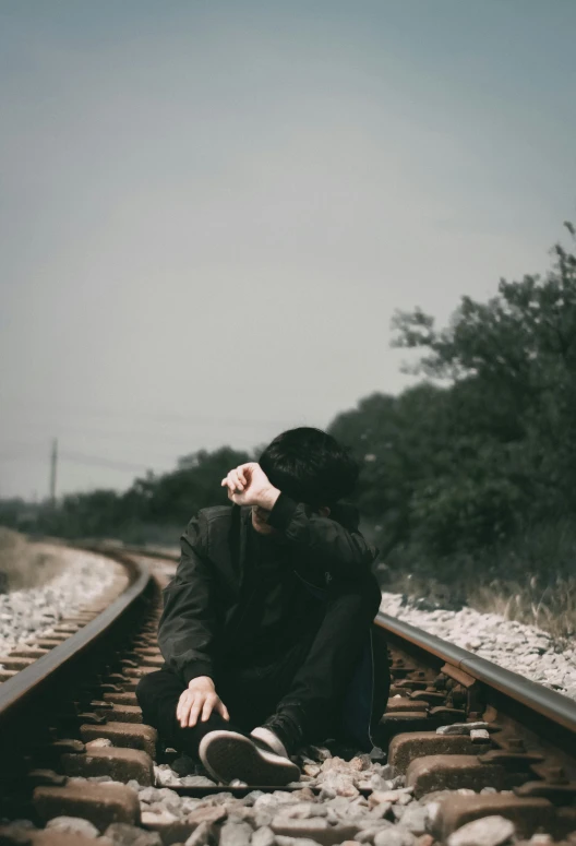 a woman sits on train tracks, with her head tilted to the left