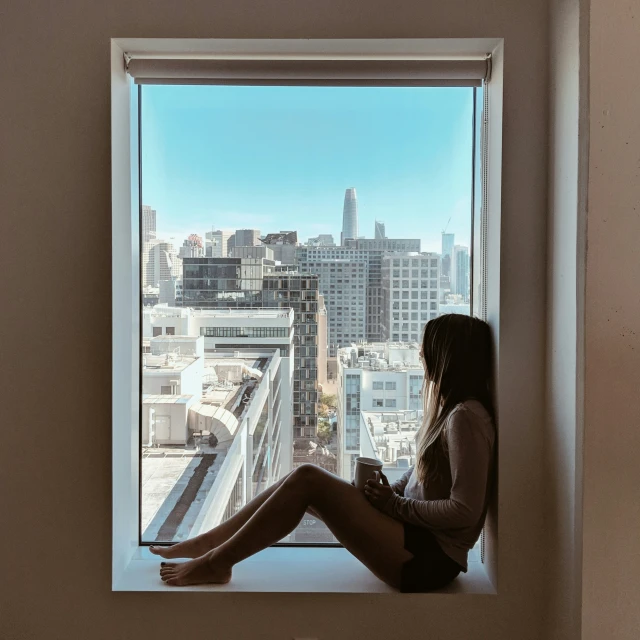 a woman sits on the ledge of a window in the city