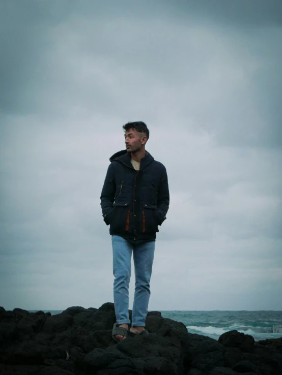 man standing on rock by ocean under stormy sky