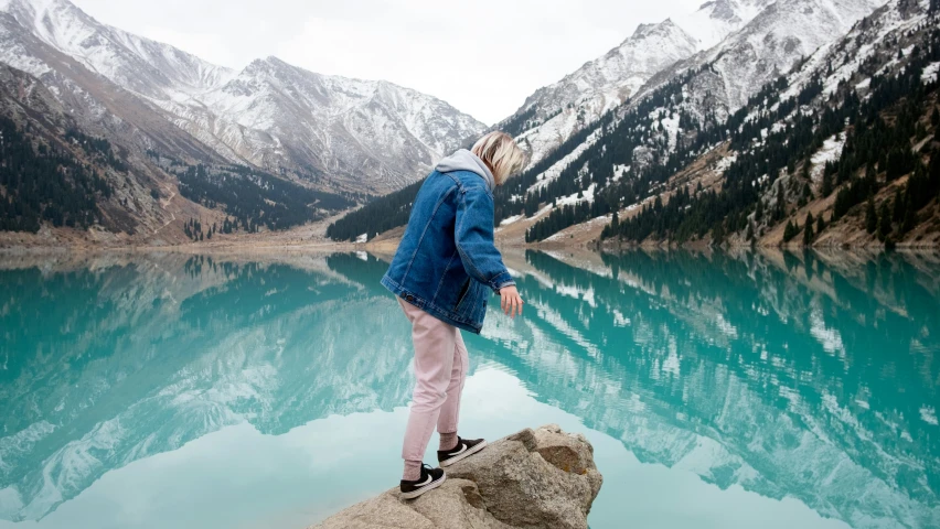 a girl wearing a blue jacket looks into the distance with mountains in the background