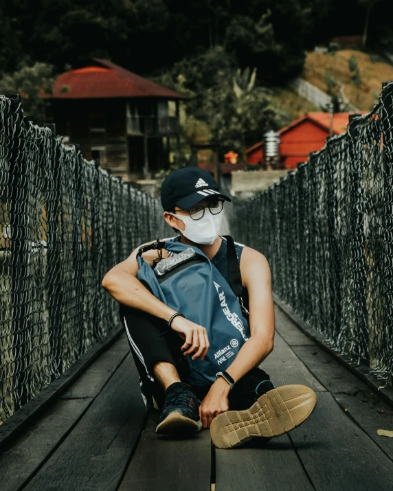 man sitting on a bridge wearing a face mask