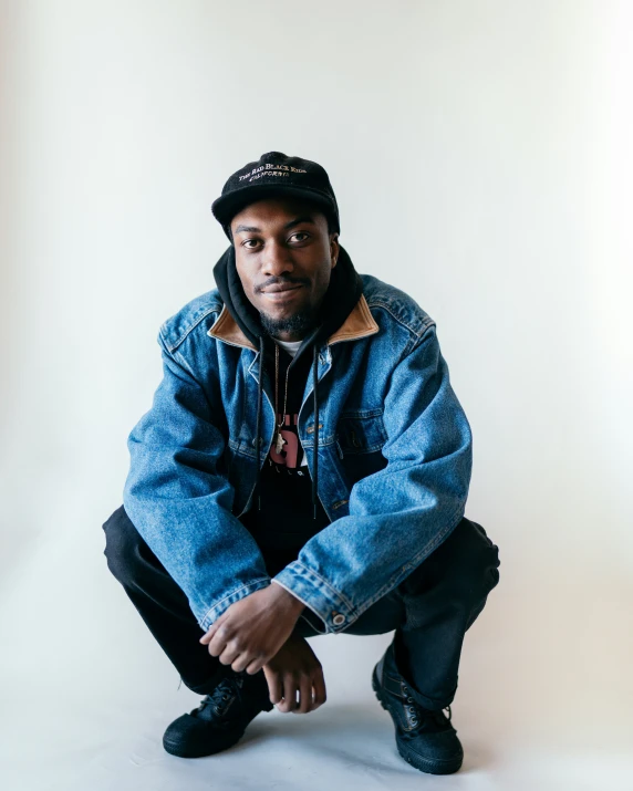 a young man is posed wearing a jean jacket and hat