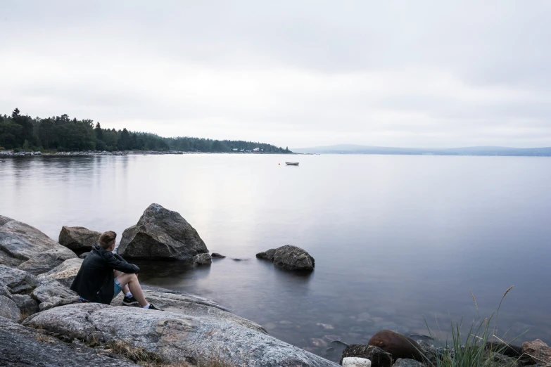 a man sitting on top of a rocky shoreline by the water