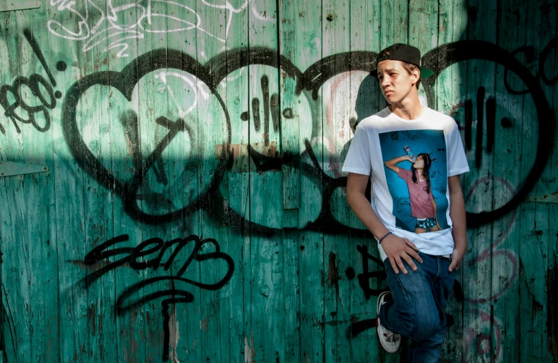 a young man standing by a wall with graffiti on it