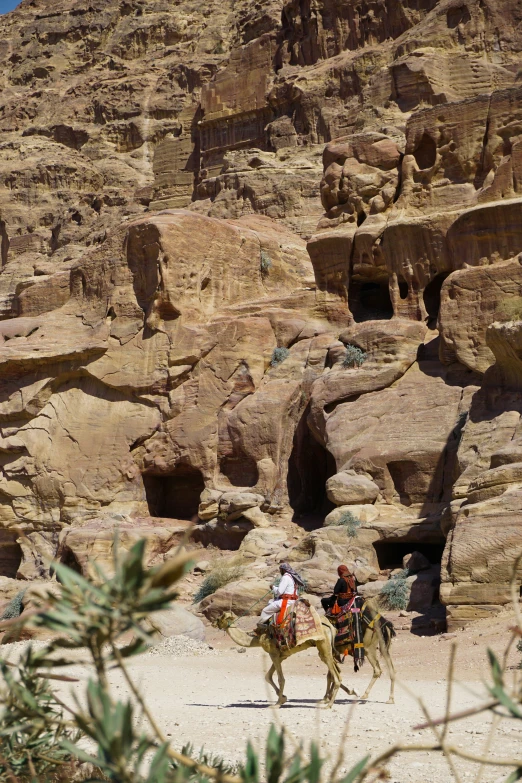 two people riding horses through a rocky landscape