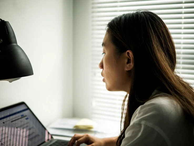 a woman working on a laptop next to a lamp