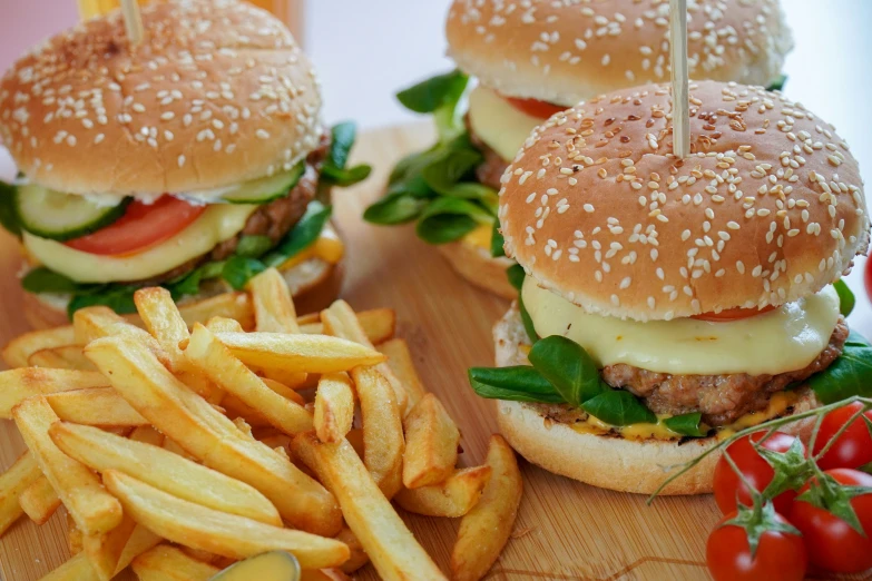 burgers and french fries on wooden  board next to vegetables