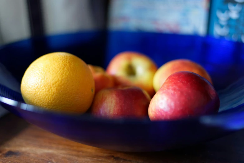 a blue bowl holding oranges and apples on a table
