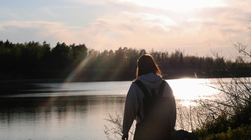 the woman is walking away from the lake and her hair is blowing