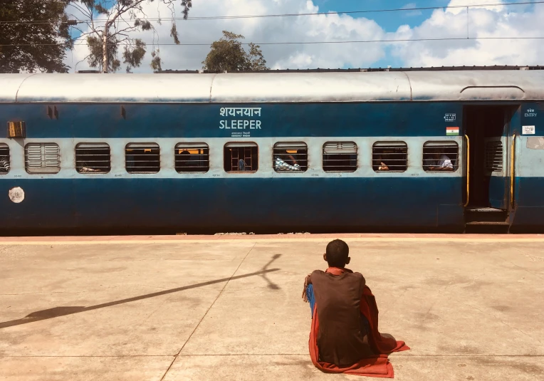 a person sitting on the ground looking at a train