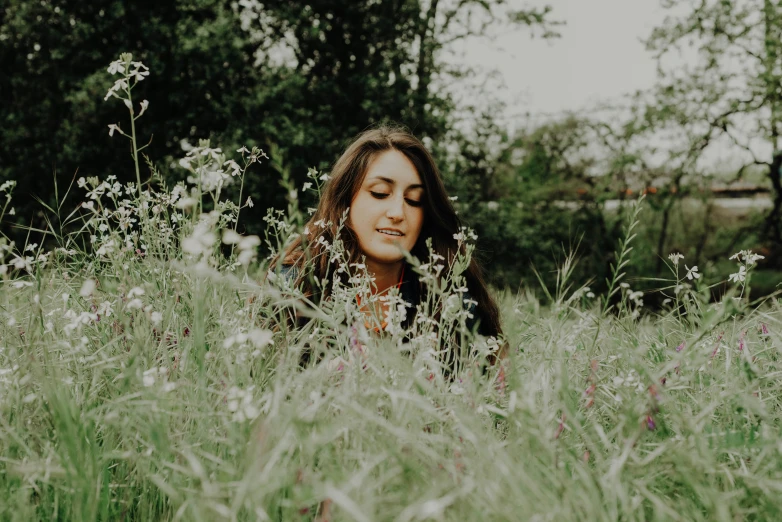 a woman sitting in some tall grass on top of a field