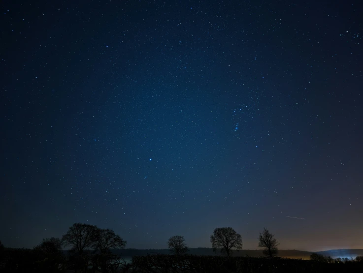 the night sky with stars, trees and a river