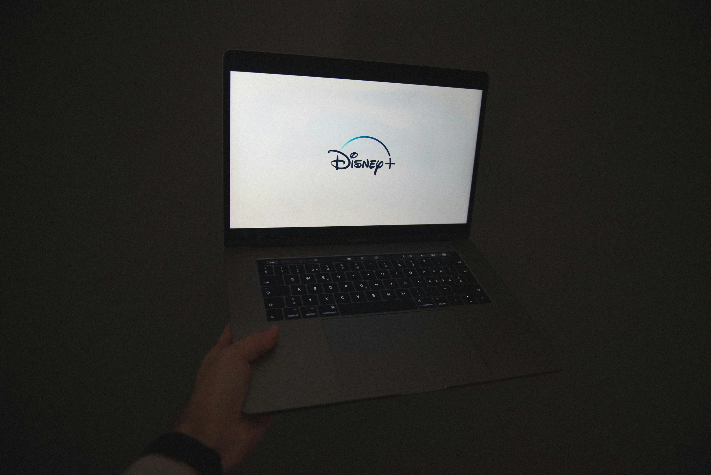 a laptop sitting in the dark with a person holding the laptop and a hand