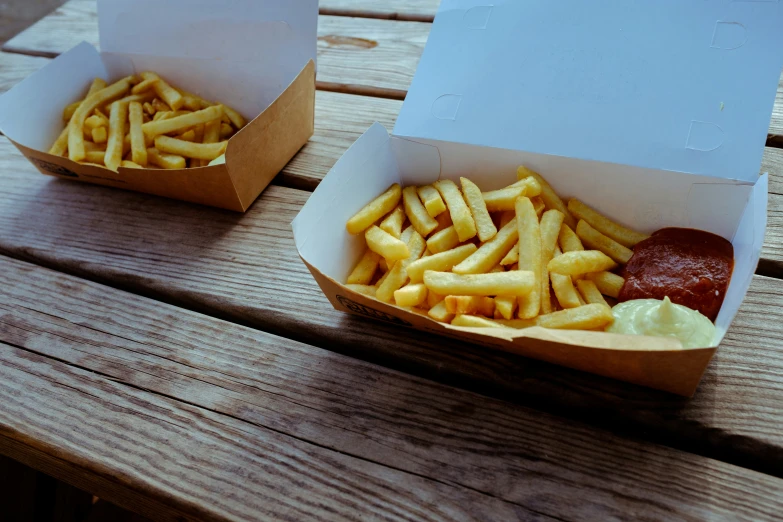 two boxes with fries, ketchup and mustard on a wooden bench