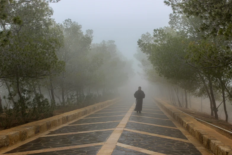 person in black robe walking down paved street on a rainy day