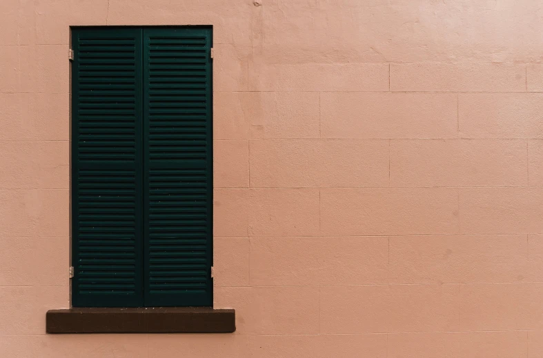 the side of a pink wall with a green shutter