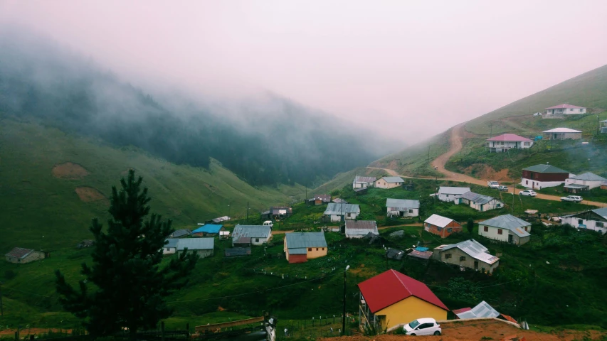 a small village on a grassy hill with mountains in the background