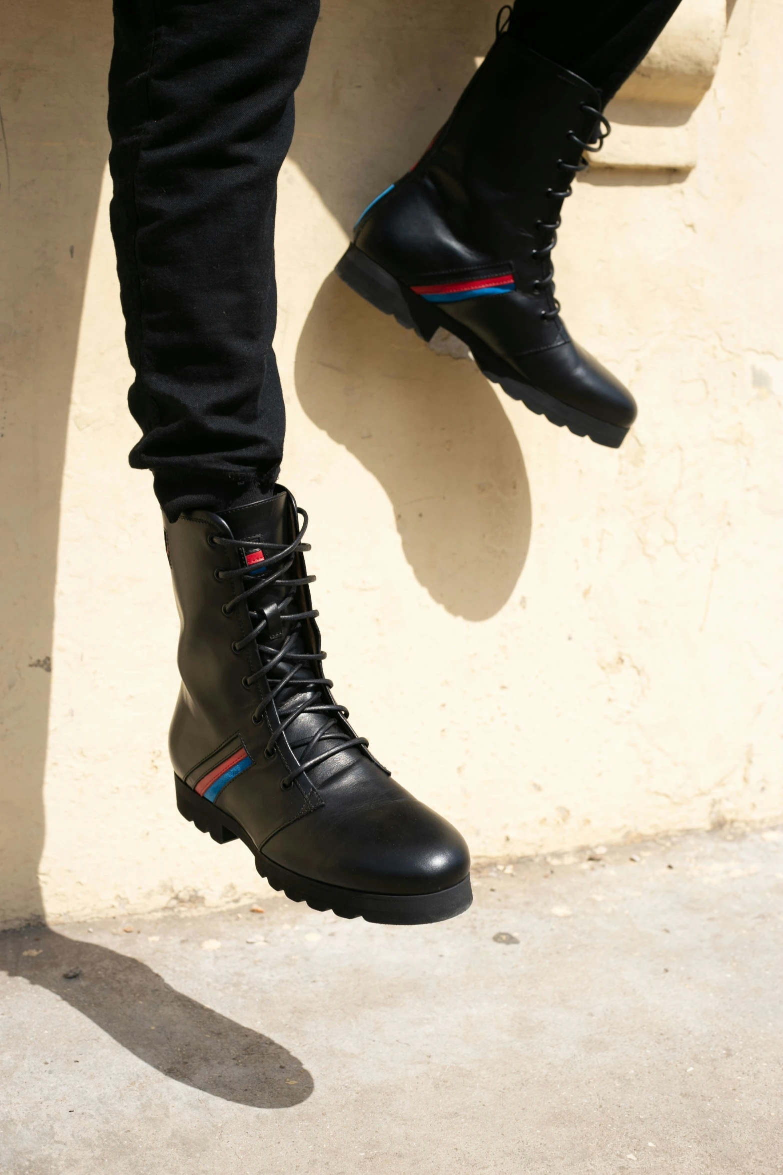 a man in black boots with black jeans and leggings standing near a cement wall