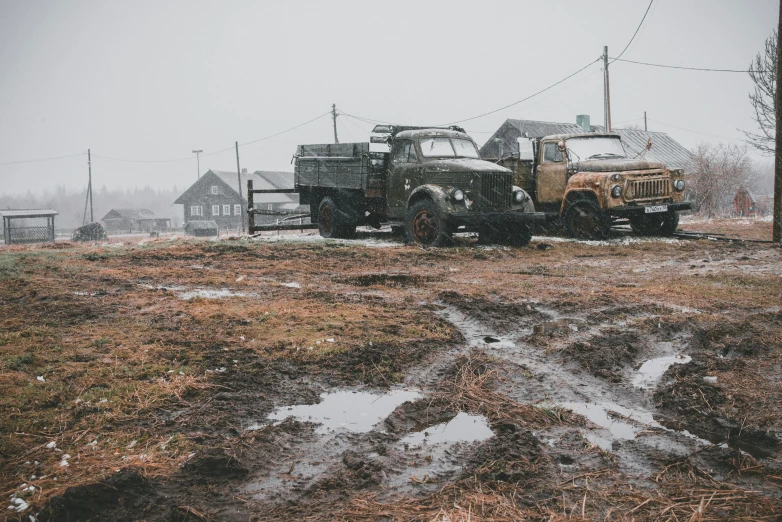 two army vehicles parked on dirt near some houses