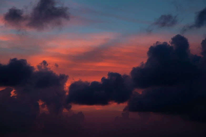 the silhouette of several clouds at dusk