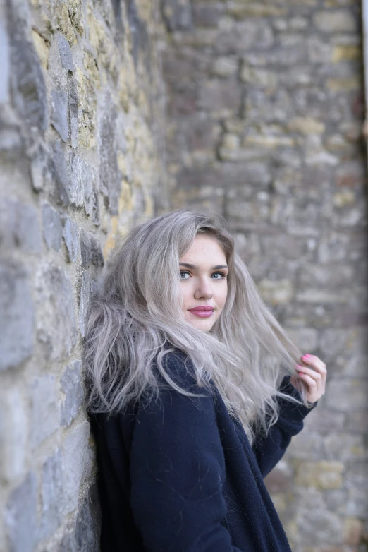 a woman with long white hair leaning against a stone wall