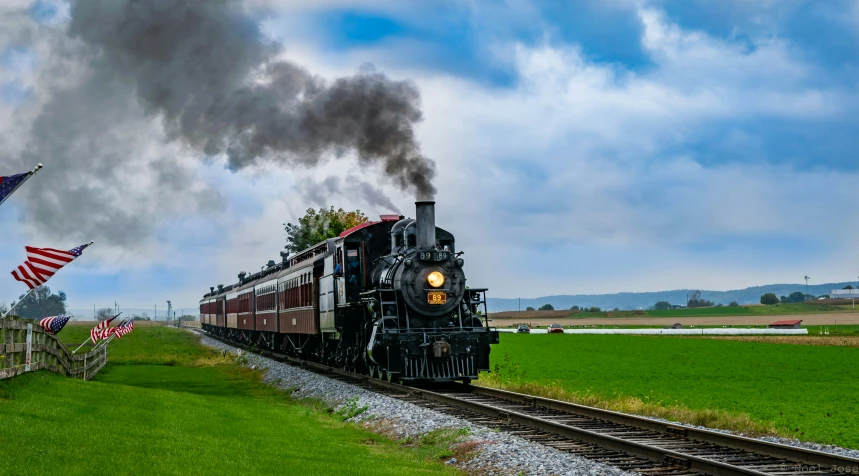 an old fashioned train on the tracks and several american flags flying