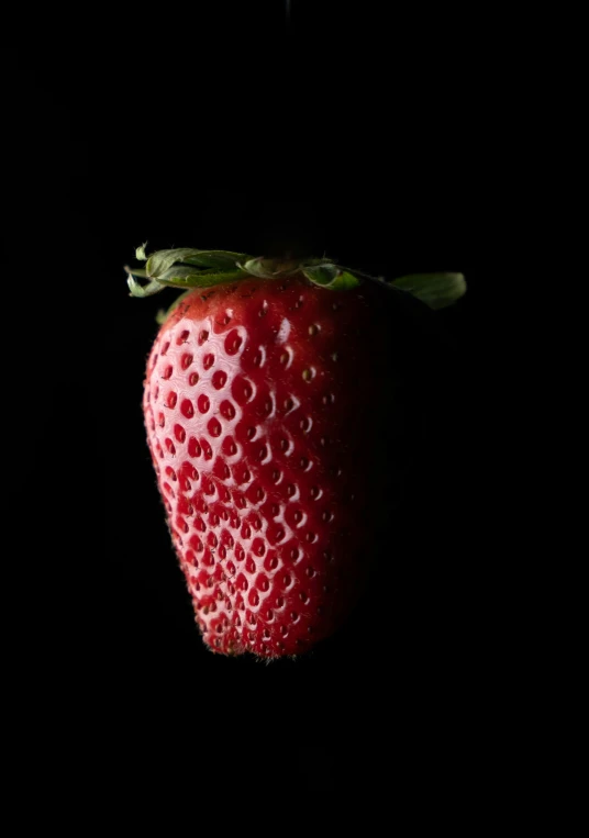 a ripe strawberry with a green stalk laying on top of it