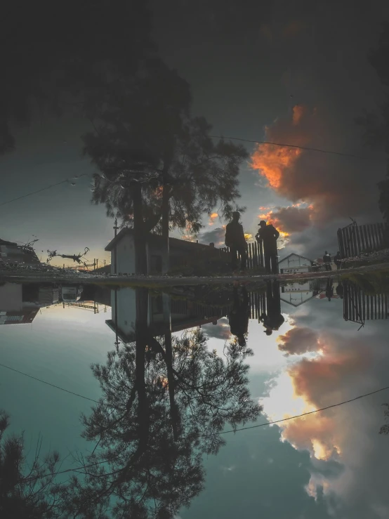 two people stand on a fence by the river with their reflection in the water