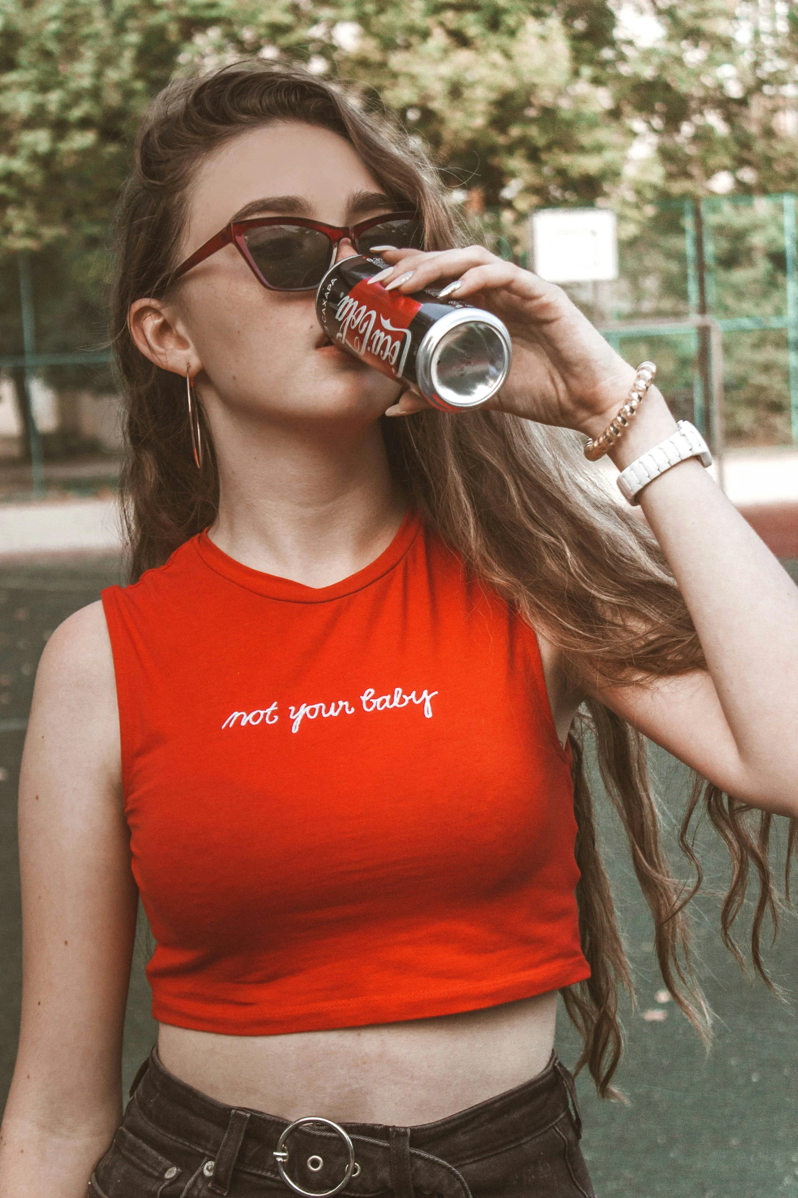 a woman is drinking a coca - cola while wearing a crop top