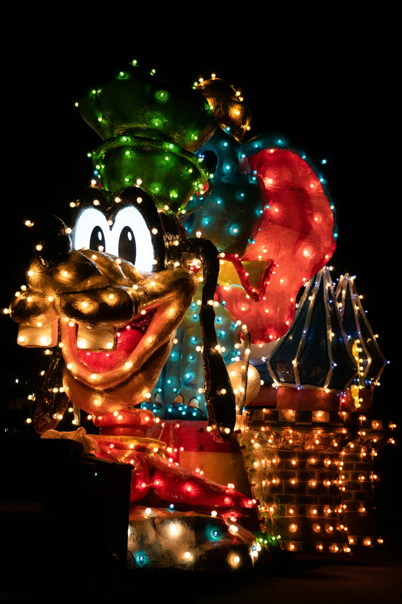 mickey mouse is lit up at night with christmas lights