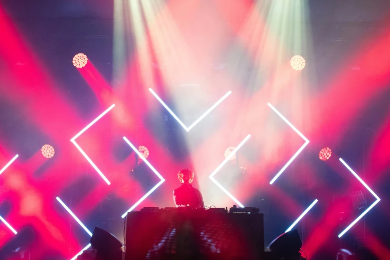 a dj performing on a stage in front of a red, pink and white background