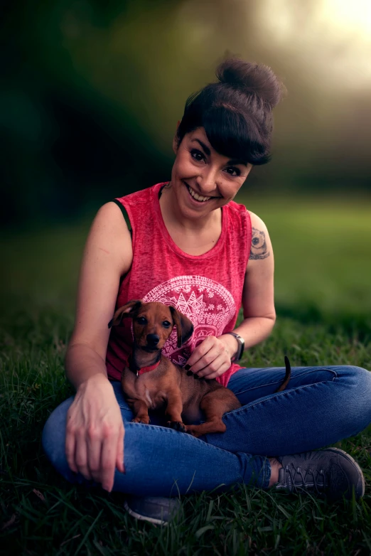 a woman sitting in the grass holding her little puppy