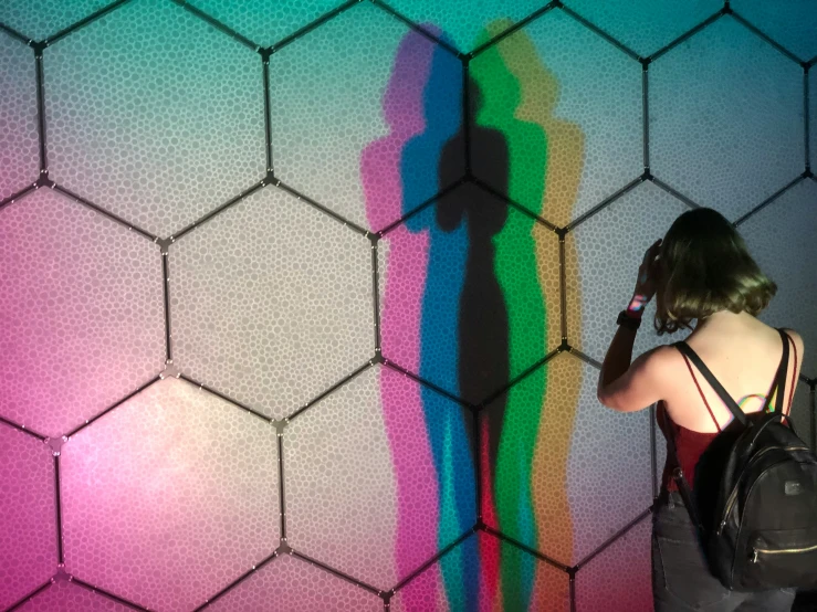 a woman is on her cellphone while she stands in front of the colorful pattern